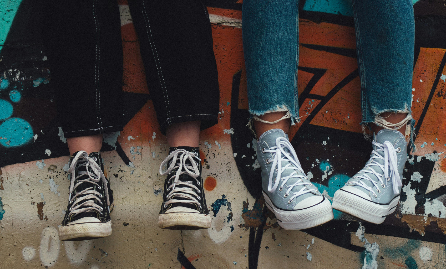 zwei Paar Beine mit Schuhen der Marke Chuck Tailor als Symbol für Jugendlich